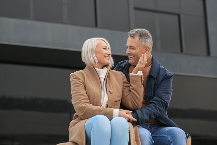 A middle age couple sitting on the steps of a building appearing very loving together.