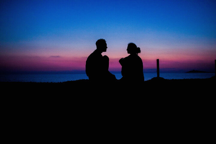 A couple sitting on a hilltop watching a sunset together while engaged in deep conversation