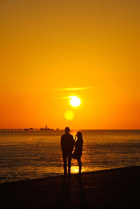 A man and woman standing on a beach watching the sunset together