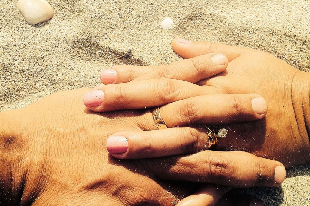 Male and female hands touching in beach sand.